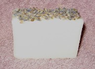 A beautiful bar of Truly Lavender Soap is pictured with organic lavender buds; a rich and creamy vegan bar, a good choice for dry or sensitive skin.